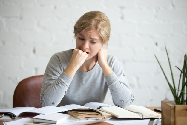 retrato-muchacha-estudiante-que-sienta-escritorio-que-muerde-su-puno_1163-2568